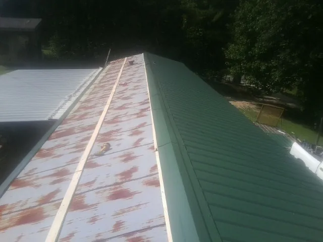 Old rusted panels beside newly installed green metal roofing — Wind Damage Roof Repair by Roofing Brothers in Rainier