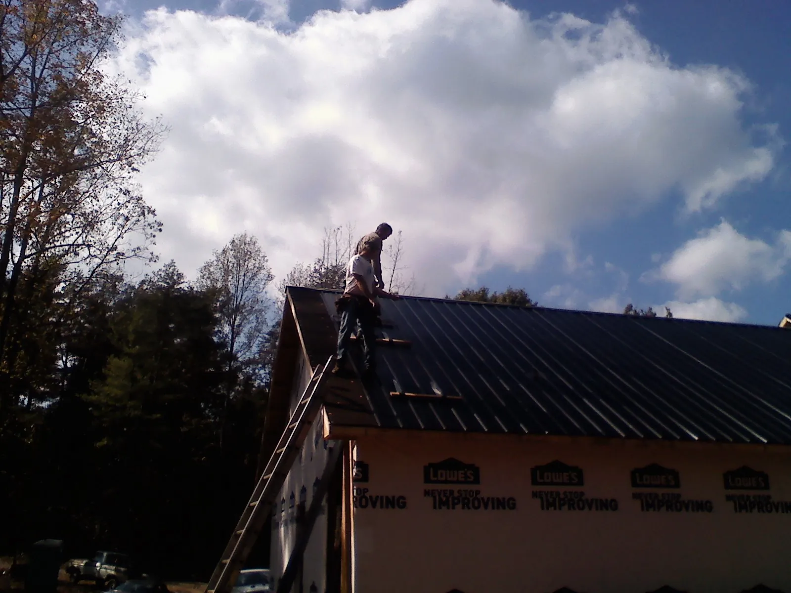 Roofer fastening dark metal panels high against a cloudy sky, from a Roof Inspection job in Rainier