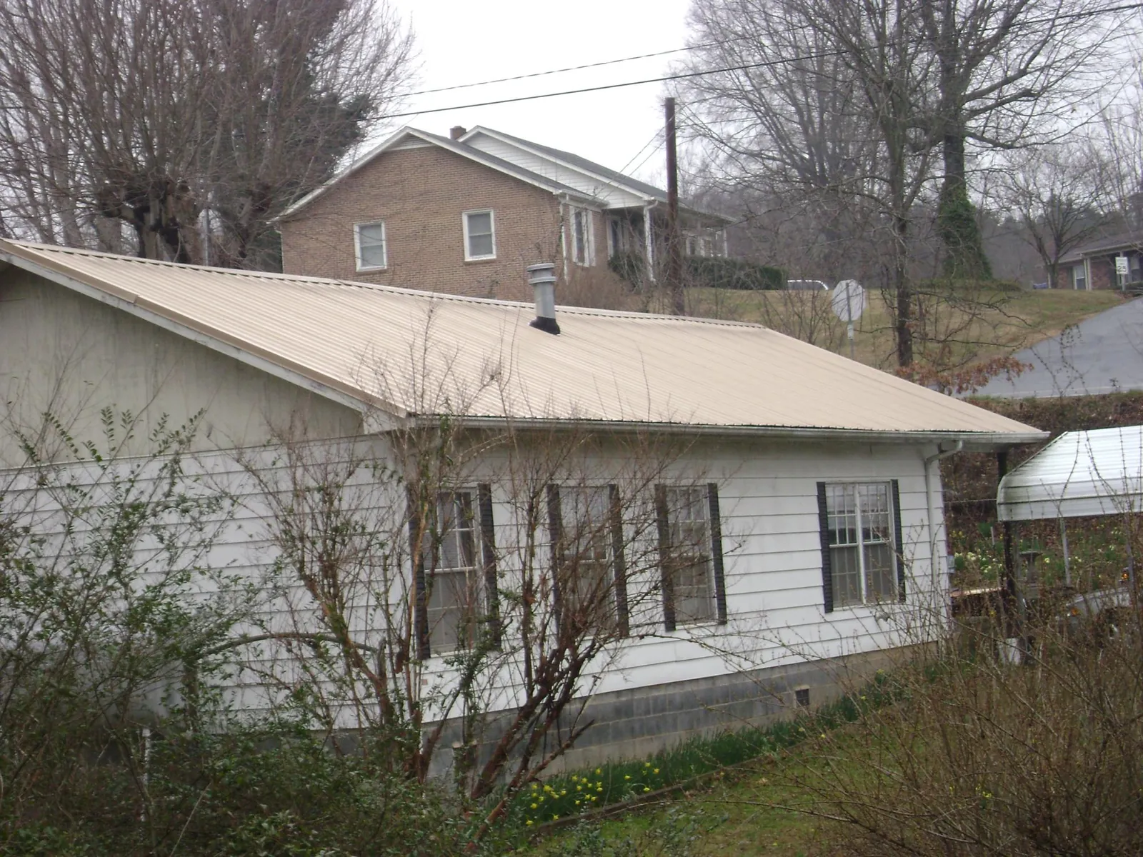 Tan metal roof on a white sided house set into a hillside — Commercial Roofing by Roofing Brothers in Rainier